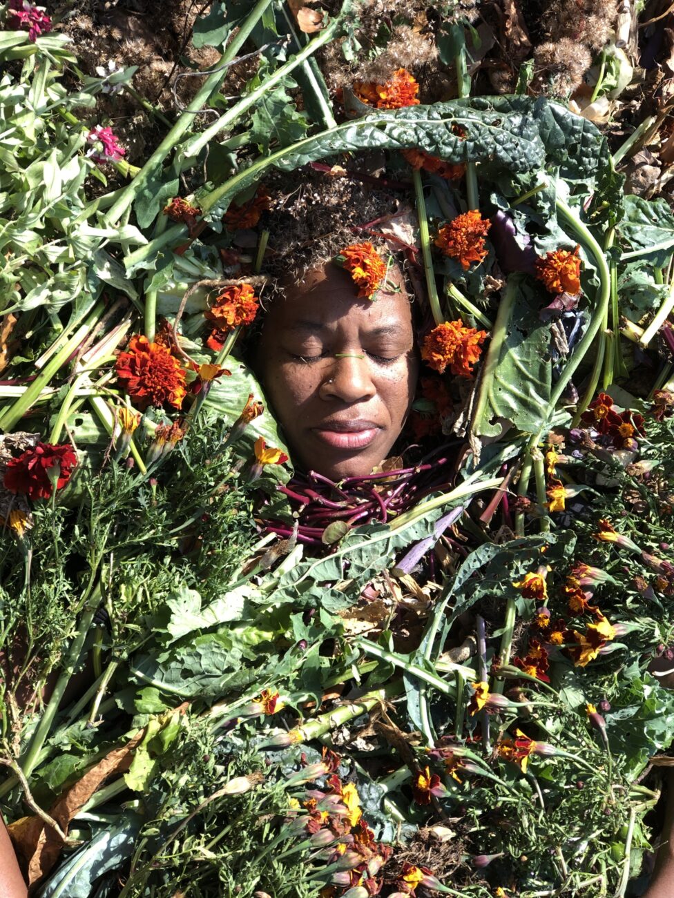 Colorful image of a person submerged in plants and marigolds. 