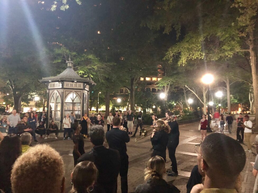 People in a public space gathering around a band of horn players. 