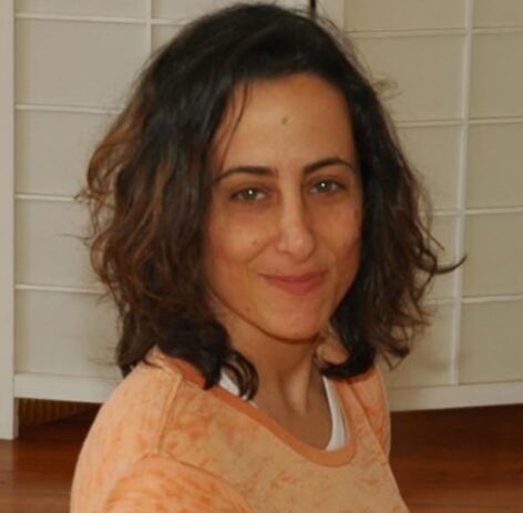 Headshot of Jen Harmon. She has dark wavy hair and wears a light orange top. She looks into the camera with a grin. Photo courtesy of the artist. 