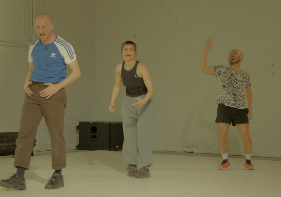 Three dancers stand, emoting, in a well-lit room. 