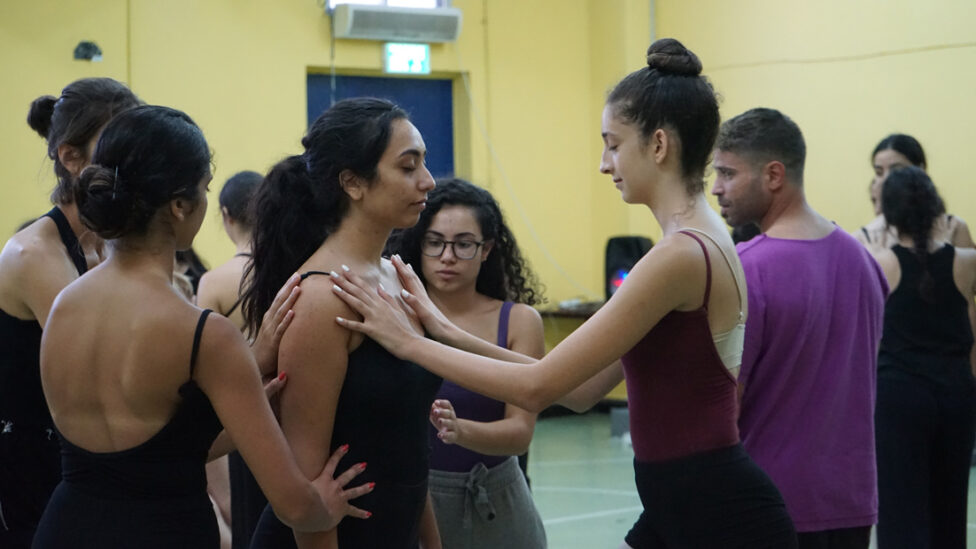 Dancers in leotards close their eyes and place their hands on one dancer towards the center. 