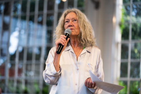 Sara Shelton Mann wears a white shirt and speaks into a microphone. Photo by Robbie Sweeney.