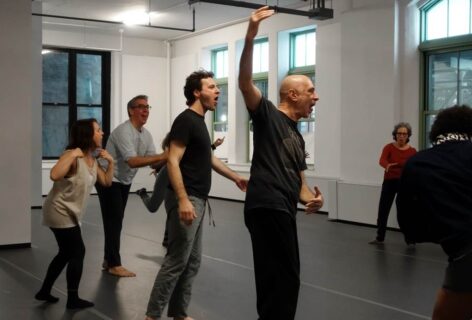 Several people stand around a circle inside of Movement Research's studio, gesturing in different ways and leaning forward with their tongues out. Photo by Harry Shunyao Zhang.