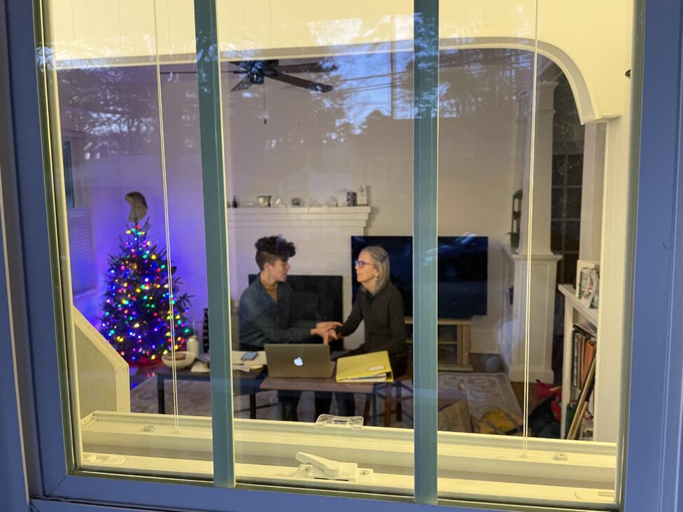 Through a glass, we can see Annie and Leah plan an experiential anatomy workshop. Photo credit: em pike