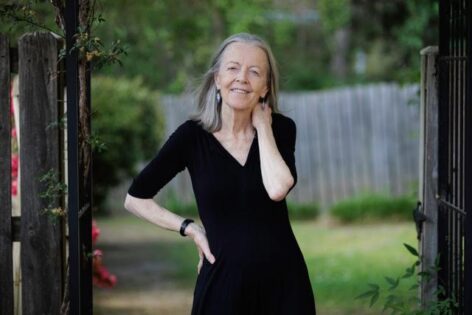 Annie, a white woman wearing a black dress, posing at the opening of the wooden gate in an outdoor setting. 