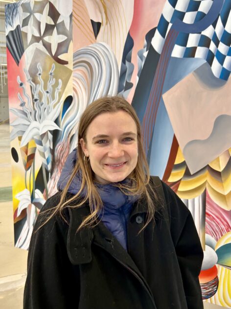Headshot of choreographer Sabina Bočková dressed in black coat in front of colorful background and smiling. Photo by Lukáš Palán