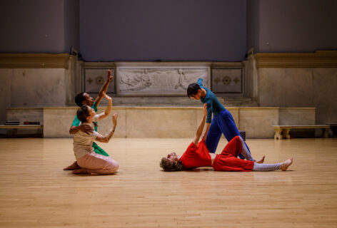 A photo from Jade Manns' performance for Movement Research at the Judson Church; two dancers kneel and gesture with their arms reaching upward and their palms facing out; two other dancers are engaged in a movement; one dancer wearing red lies on the floor and reaches towards the second dancer wearing blue, and the second dancer leans over pulling the first dancers shirt. Photo by Rachel Keane