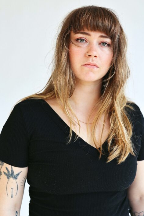 Abbey stands facing the camera wearing a black shirt. She has blonde hair and bangs. Photo by Sam Pickart