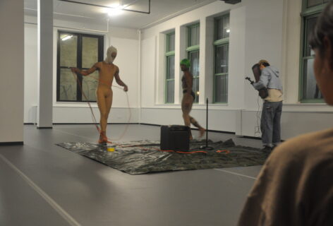 Three performers set up on a square tarp, they have cords and a large amp in the center of them. Artists are unknown. Photo by Mary Anne Bodnar.