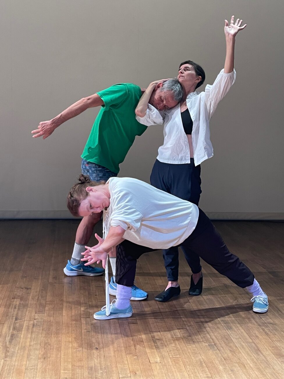 Three figures pose together, forming an asymmetrical shape. Two of the figures stand with arms protruding outward, while the third lunges below them. Photo credit to Deborah Hay.