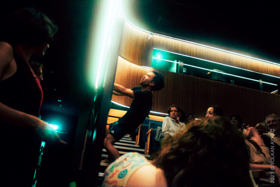 Julian hanging onto a wall in performance, leaning backwards. Image by Volkan Aykac.