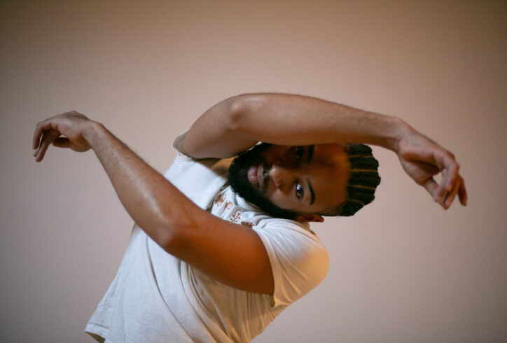 A black man stare into the camera with his right arm crossed over the left. The top of his head leans towards his left. Photo by Whitney Browne