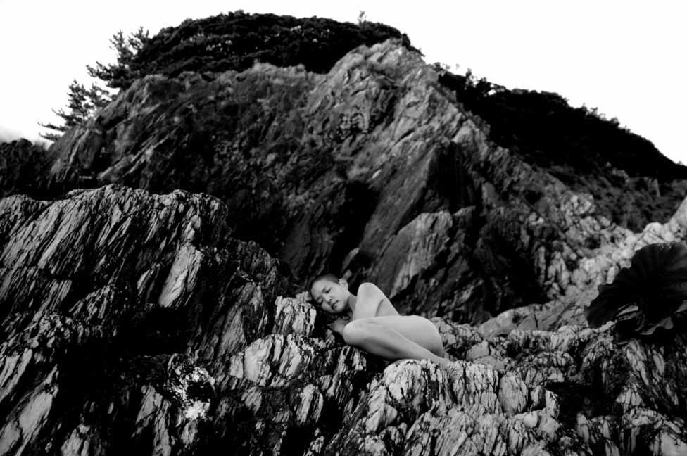 Black and white photo of kyoko laying on a rocky hill. Photo by Andre Shizen.