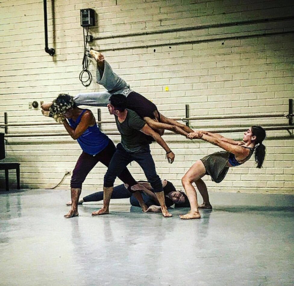 A group of dancers in a shape. The figure on the right-most side pulls and leans away from a dancer being lifted in the air, creating a feeling of suspense and balance. The group is practicing extreme counter-balance using different levels. From left to right: Ariel Green-Hill, Irvin Manuel Gonzalez, Rosa Rodriguez-Frazier, Tracy Tom-Hoon, Elizabeth Villalobos