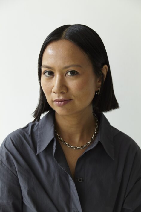 A portrait of an Asian woman with short black hair and blue dress in front of white background. Photo by Isabel Asha Penzlien.