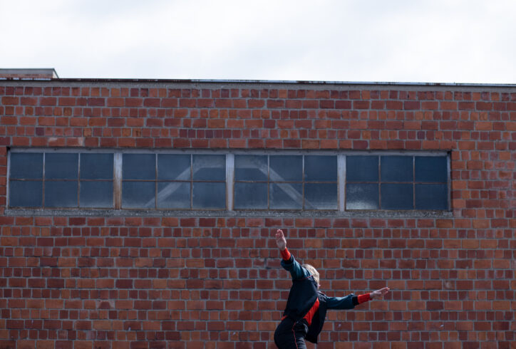 Exterior landscape consisting of a brick building in the background and a dancer in the foreground. Image by Ivan Idžotić.