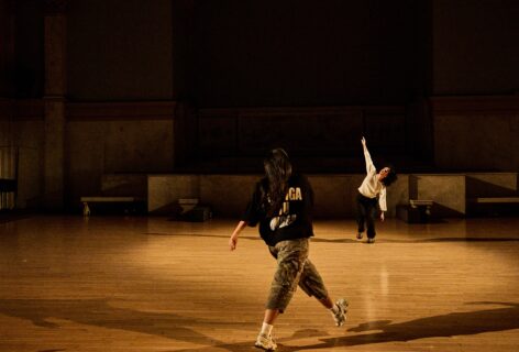 A photo from Aleeza Garcia's piece for Movement Research at the Judson Church. Two dancers move around the space one takes a wide step forward. The other slices their arm through the air. Photo by Ryutaro Mishima.