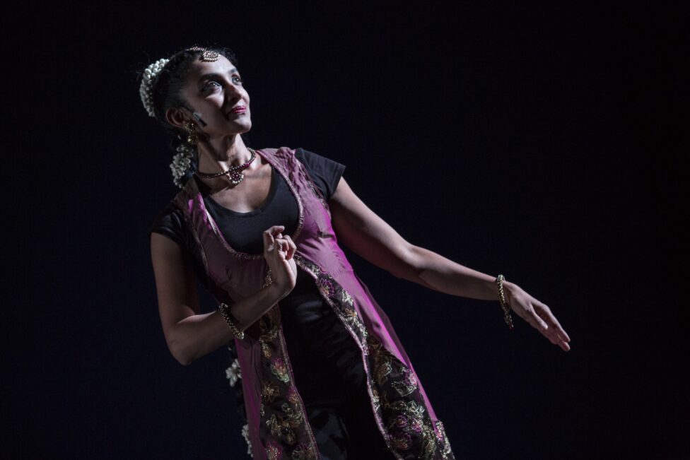 Preeti Vasudevan in Stories by Hand. Medium-toned woman looks upwards wearing a purple vested outfit and flowers in her bun. Photo credit: Marina Baranova
