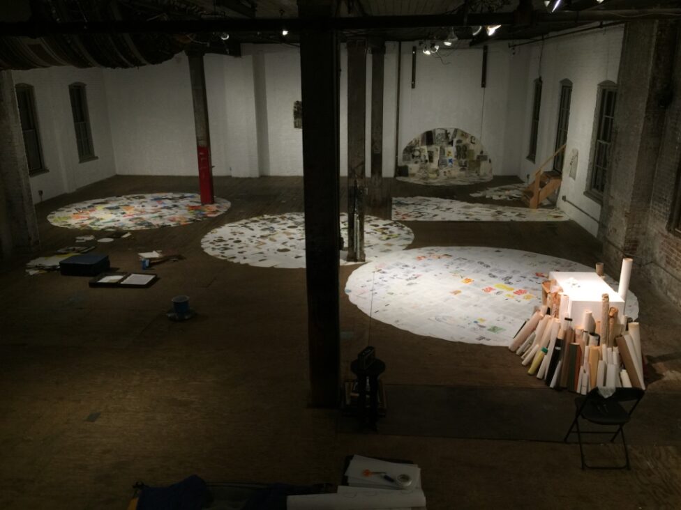 An installation image of Atlantic Terminus by Jon Kizel at Invisible Dog in 2016. The image shows a performance space with three circles of paper on the ground. Columns support the ceiling.