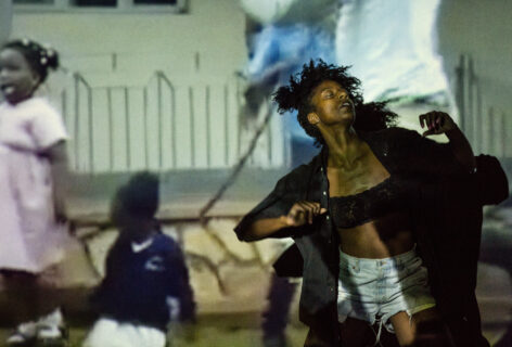 Marguerite's head is tilted back with eyes closed as she dances in front of a projection of Black youth dancing. Image by Scott Shaw.
